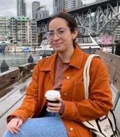 young non-binary editor in an orange jacket holding a coffee