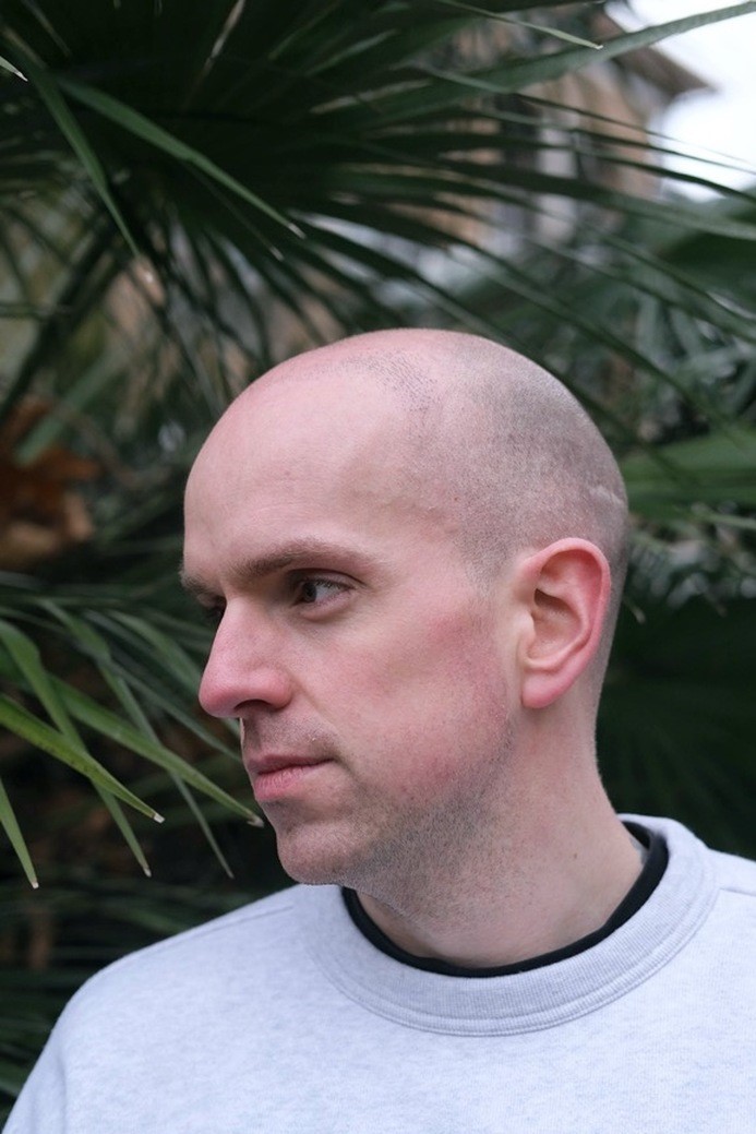 A portrait of the author, in front of green foliage