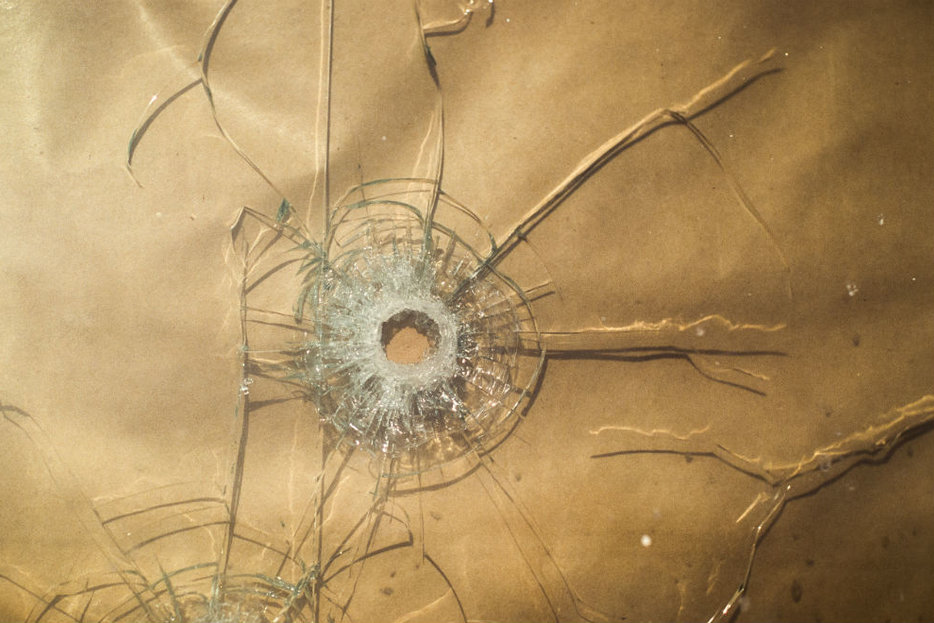 Image of glass shattered by a bullet hole with cracks radiating outward. Glass has tan paper behind it.