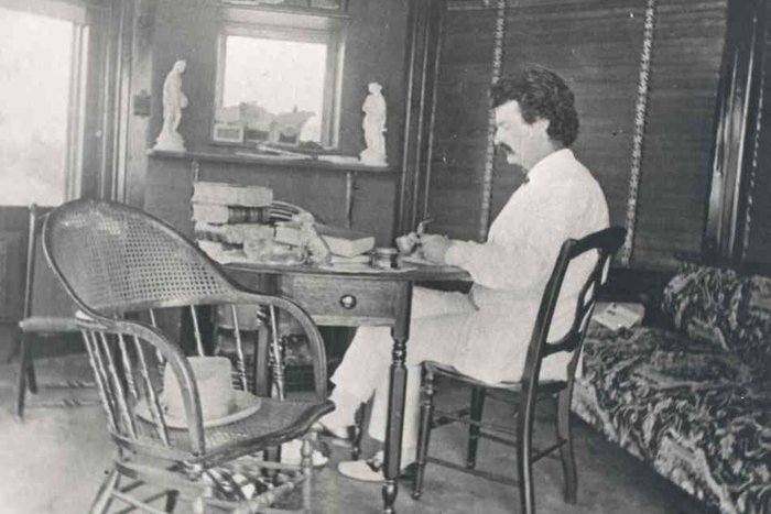 || Mark Twain sitting at his desk.