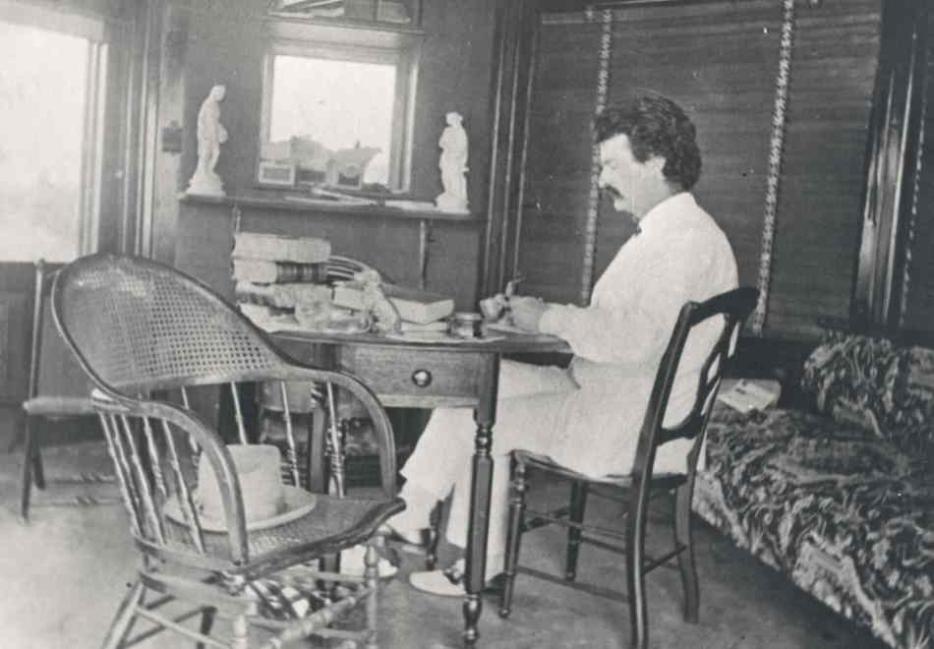 || Mark Twain sitting at his desk.