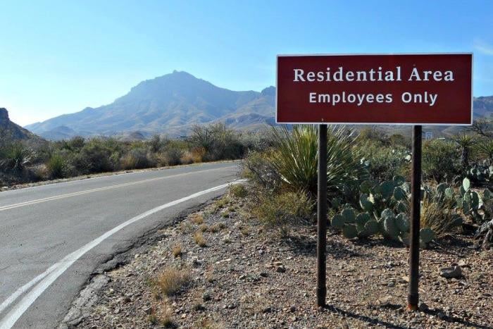 An employees-only sign beside a road in Big Ben National Park. There are mountains in the background. 